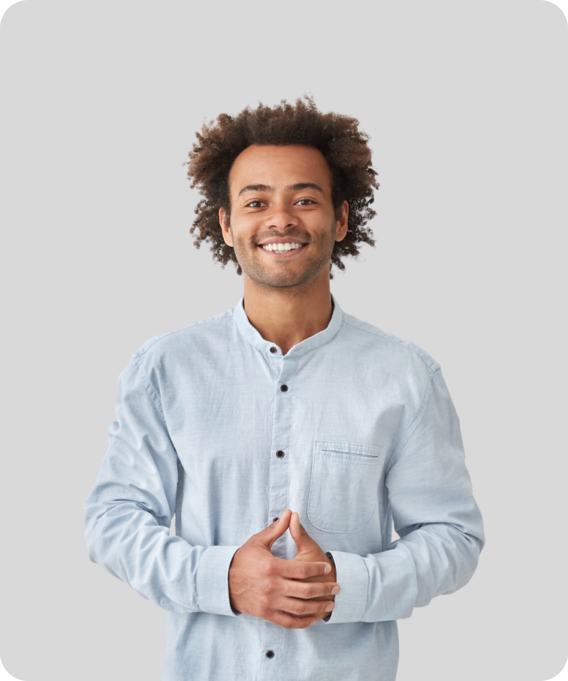  Smiling young man in a light blue shirt with curly hair standing against a plain background