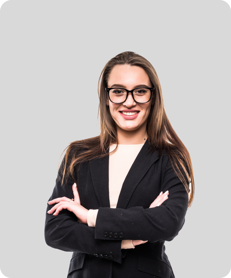 Confident young woman in glasses and a black blazer smiling with arms crossed against a light grey background